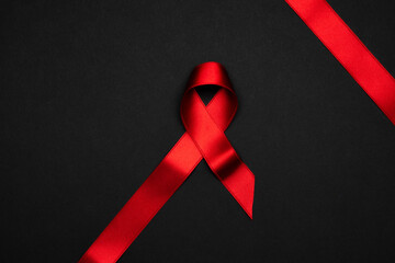 Aid ribbon silk. Red ribbon symbol in hiv world day on black background. Awareness aids and cancer. Flat lay, top view, copy space