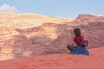 Fototapeta na wymiar a girl sits on the edge of a sand dune in front of a relief mountain, nature jordan