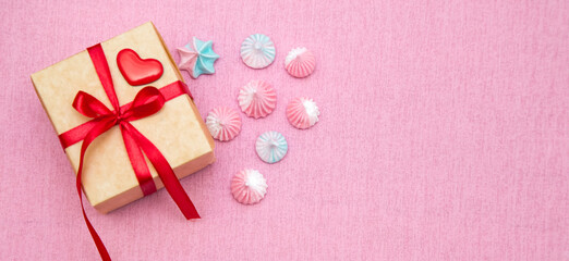 gift box with red ribbon on pink background and heart shaped lollipop