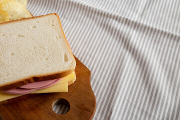 Homemade Bologna and Cheese Sandwich on a rustic wooden board on cloth, side view. Space for text.