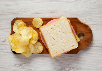 Homemade Bologna and Cheese Sandwich on a rustic wooden board on a white wooden background, overhead view. Flat lay, top view, from above.