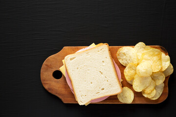 Homemade Bologna and Cheese Sandwich on a rustic wooden board on a black surface, top view. Copy space. © Liudmyla