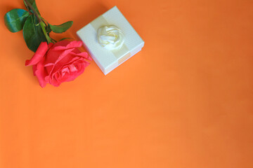 Red rose and white gift box on an orange background, flat lay, copy space