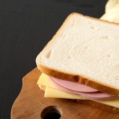 Homemade Bologna and Cheese Sandwich on a rustic wooden board on a black background, side view. Copy space.