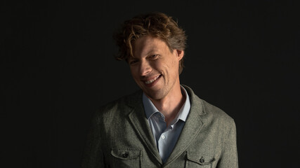 Grimacing face young man in jacket makes funny bewildered face looking at camera isolated on black background. Studio shot. Facial expressions, emotions, feelings.