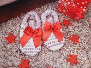 Fototapeta na wymiar Christmas background of white soft home slippers and red Christmas decoration with gift boxes. Flat lay, top view. New Years gift ideas.