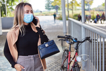 Naklejka na ściany i meble Woman with face mask because of Covid-19 and smartphone