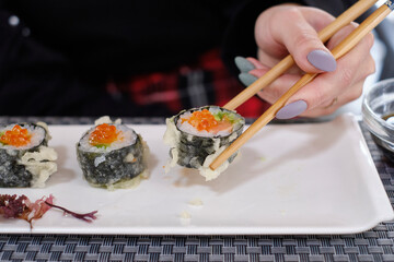 Gunkan Sushi with salmon roe on a white plate with Japanese chopsticks.