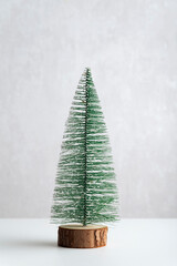 Miniature artificial Christmas tree on wooden stand on white background. Vertical frame