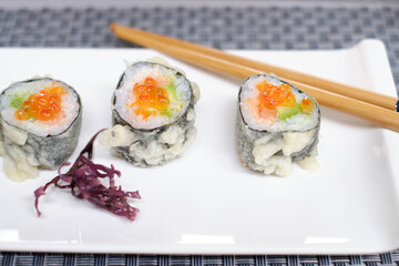 Gunkan Sushi with salmon roe on a white plate with Japanese chopsticks.