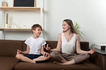 Mother teach a son meditate sitting on couch. Yoga at home with children.
