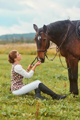 Girl sitting on the grass and stroking her horse