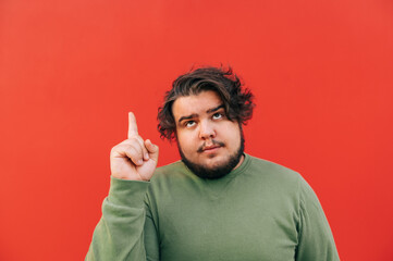 Portrait of a thoughtful corpulent bearded hispanic guy expressing an idea gesture by pointing his...