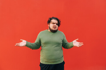 Confused overweight bearded hispanic man is throwing his hands up is despair, feeling annoyed and...