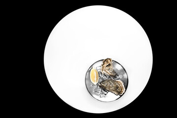 Fresh Closed Oysters, Ice, Lemon On A Round Metal Plate  On A white round table on black background. two oysters on a plate on a white round table. view from above