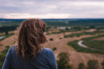 Fototapeta premium the girl sits on a hill and has a beautiful view of the river and fields in front of her