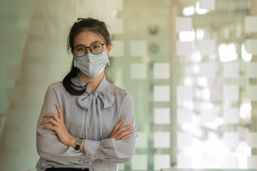 Fototapeta na wymiar Business Asian women stand and wear masks and cross arms in the office.