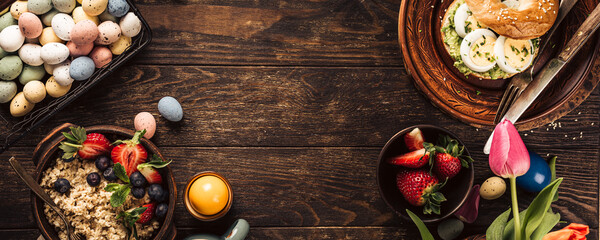 Rustic easter breakfast flat lay with eggs bagels, tulips, croissants, egg, oatmeal with berries, colored quail eggs and spring holidays decorations. Top view, copy space. Banner