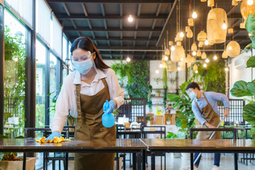 Portrait attractive Asian restaurant employee wear face mask and face shield cleaning table and floor with alcohol and wet wipe before welcome customer.