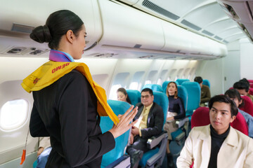 Asian Air hostess staff airline demonstrate safety procedures to passengers prior to flight take off in cabin airplane.