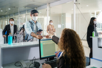 A male airline passenger with mask is handing over his passport at the airline counter check in...