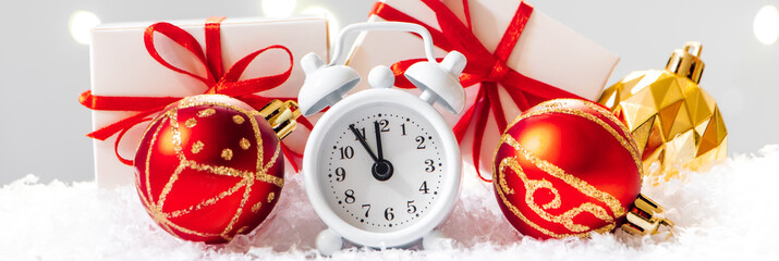 Christmas ball and alarm clock in the snow. New Year concept on background of garland lights.