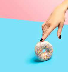 Womans hand holding colorful donut over blue background.