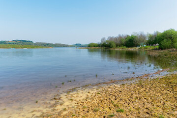 Fototapeta na wymiar On the muddy shore of Carsington Water under a blue spring sky