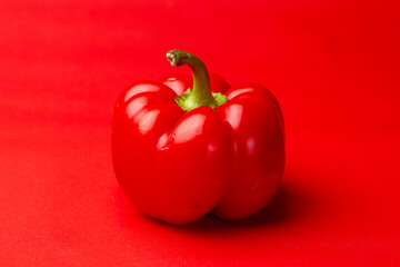 Single vibrant dark red Bell pepper or fresh paprika and green stem contrasting against an intense red clean even background