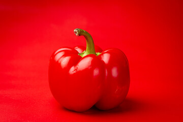 Vignette and focus on vibrant dark red Bell pepper or fresh paprika and green stem contrasting against an intense red clean even background with vignette