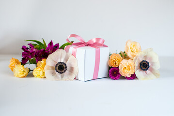 White gift box with pink ribbon with bouquet of spring flowers. Box and colorful flowers. Wedding gift presentation design, modern art. Space for text. 