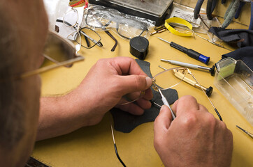 Concept of optical workshop.Expert fixing eyeglasses.Closeup of human hads, glasses, screwdrivers...