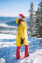 Skiing, skier, winter sports - portrait of happy young skier. Woman wearing ski outfit. Mountains, pine trees, ski resort concept.