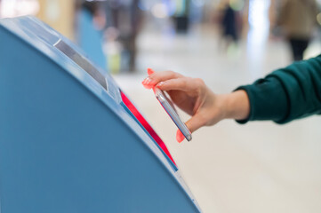 A faceless woman scans the qr code from her smartphone. A girl uses a self-service machine at the airport to check in for a flight and print tickets