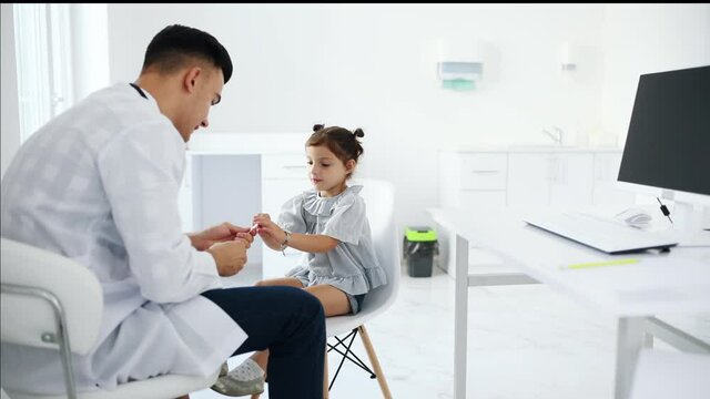 Little girl have a visit in the clinic with doctor. She taking out medical tonsil out of package.
