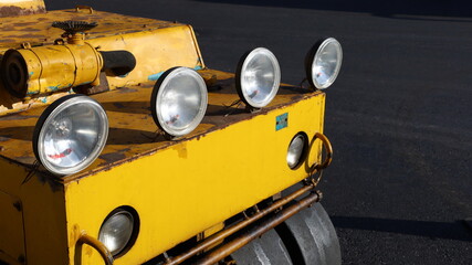 Headlights on asphalt compactors. Four round lights are supplemented on the compactor to provide light when working at night. On a paved road background with a copy area. Selective focus