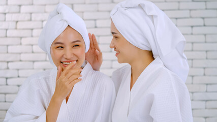 Two Asian girls in white bathrobes with towels on heads talking in living room.