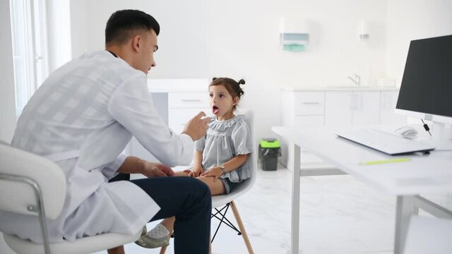Young doctor in white coat takes analizis from the little girl by using medical tonsil.