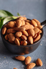 Heap of raw almonds in black ceramic bowl on stone background.