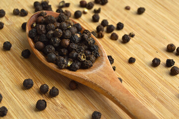 Aromatic fresh peppercorns in spoon on wooden bamboo cutting board