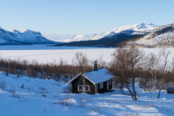 Cabin in the snow at a frozen lake in Lapland, Sweden.