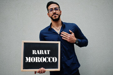 Arab man wear blue shirt and eyeglasses hold board with Rabat Morocco inscription. Largest cities in islamic world concept.
