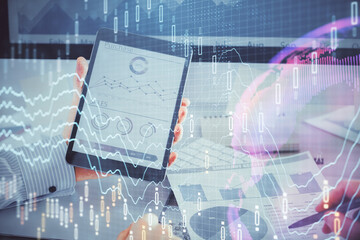 Double exposure of man's hands holding and using a digital device and forex graph drawing. Financial market concept.