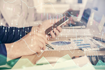 Double exposure of man's hands holding and using a digital device and forex graph drawing. Financial market concept.