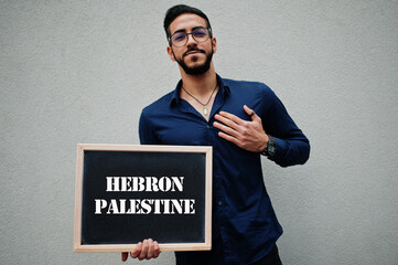 Arab man wear blue shirt and eyeglasses hold board with Hebron Palestine inscription. Largest cities in islamic world concept.