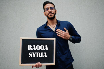 Arab man wear blue shirt and eyeglasses hold board with Raqqa Syria inscription. Largest cities in islamic world concept.