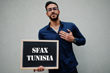 Arab man wear blue shirt and eyeglasses hold board with Sfax Tunisia inscription. Largest cities in islamic world concept.