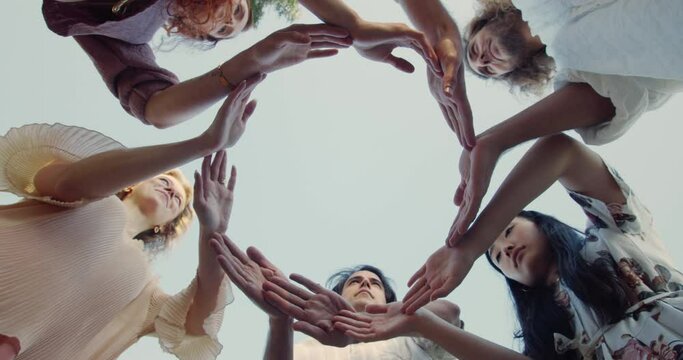 Low angle of diverse young people putting their hands in circle on sky background. Millennial friends making unity symbol of their arms and hands. Concept of togetherness