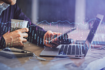 Double exposure of man's hands holding and using a phone and financial graph drawing. Analysis concept.