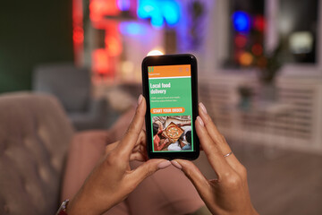 Close-up of woman holding mobile phone and ordering food online while lying on the sofa